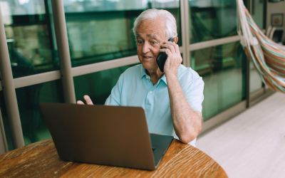 Senior siedzi przy komputerze i rozmawia przez telefon
