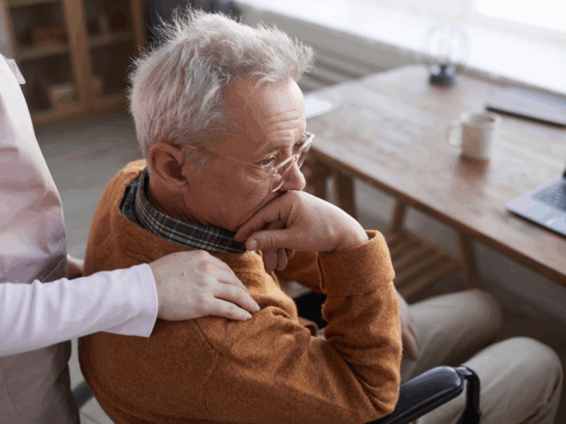 senior siedzi smutny na krześle, trzyma go inna ręka