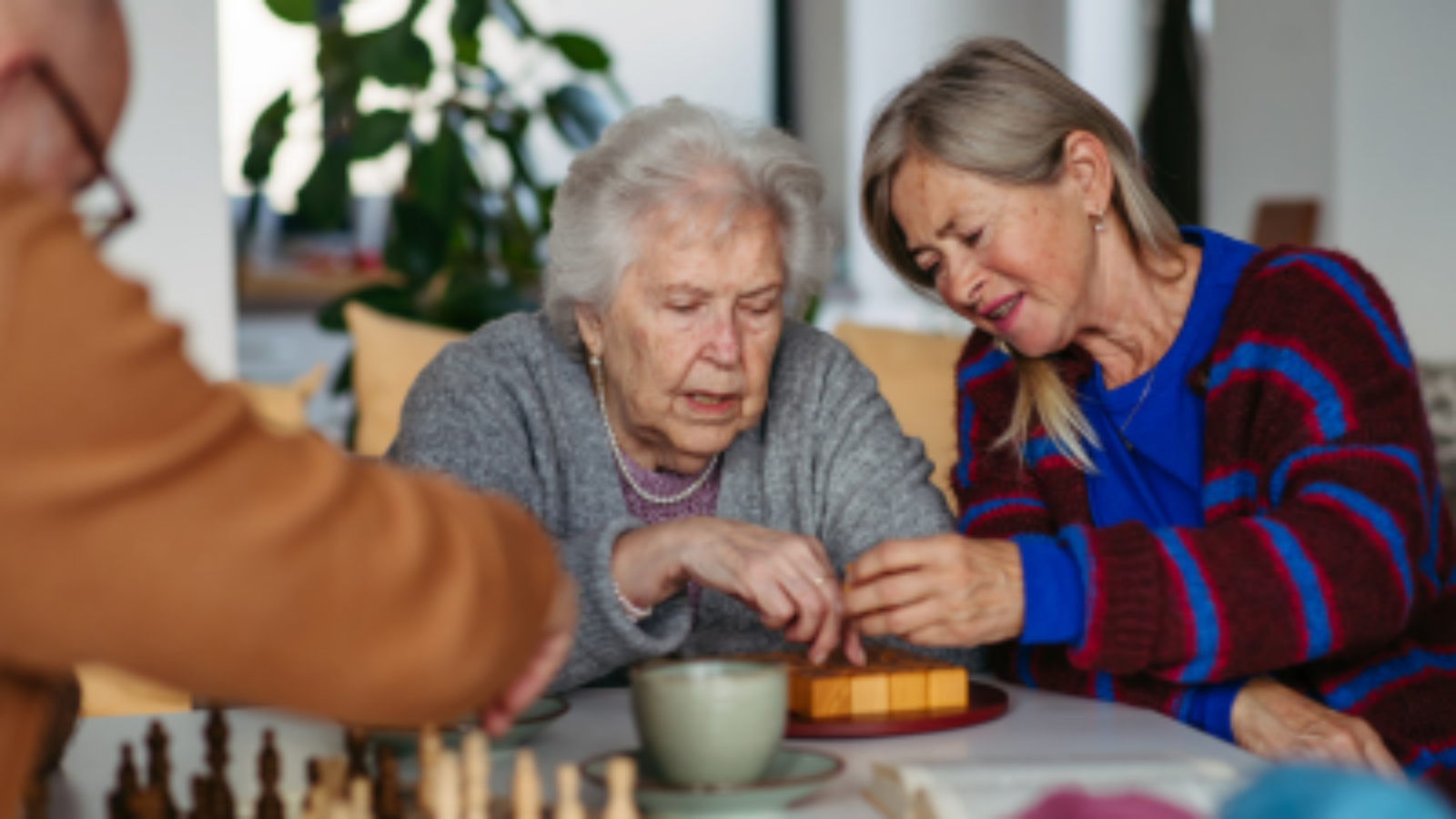 Seniorka robi jakąś układankę, druga osobajej pomaga