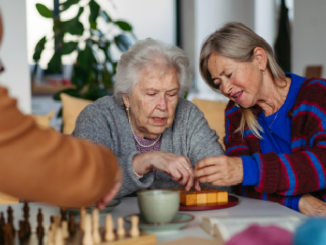 Seniorka robi jakąś układankę, druga osobajej pomaga