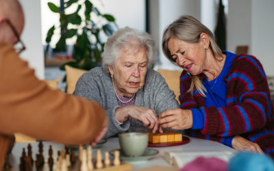 Seniorka robi jakąś układankę, druga osobajej pomaga